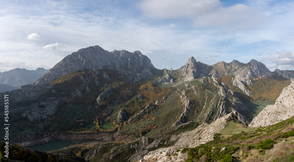Beautiful panoramic view of the mountain peaks, rocks, vegetation and trees between greenish and orange touches by autumn in the Valle de Anciles, León, Spain