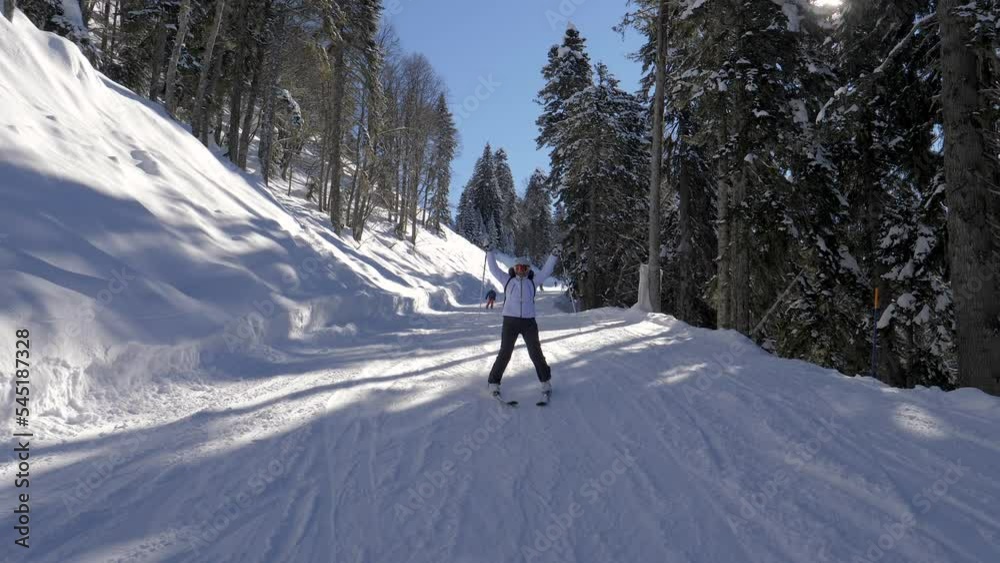 Happy smile woman skier skiing down snow slope in mountains at ski resort. Sliding on snow hilly track and pine forest. Winter recreation and sports. Raises hands up from freedom and feeling of flying Happy smile woman skier skiing down snow slope in mountains at ski resort. Sliding on snow hilly track and pine forest. Winter recreation and sports. Raises hands up from freedom and feeling of flying