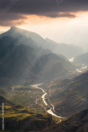 Many mountains at sunset, orange clouds, long rays of light, Dagestan. Vertical orientation.