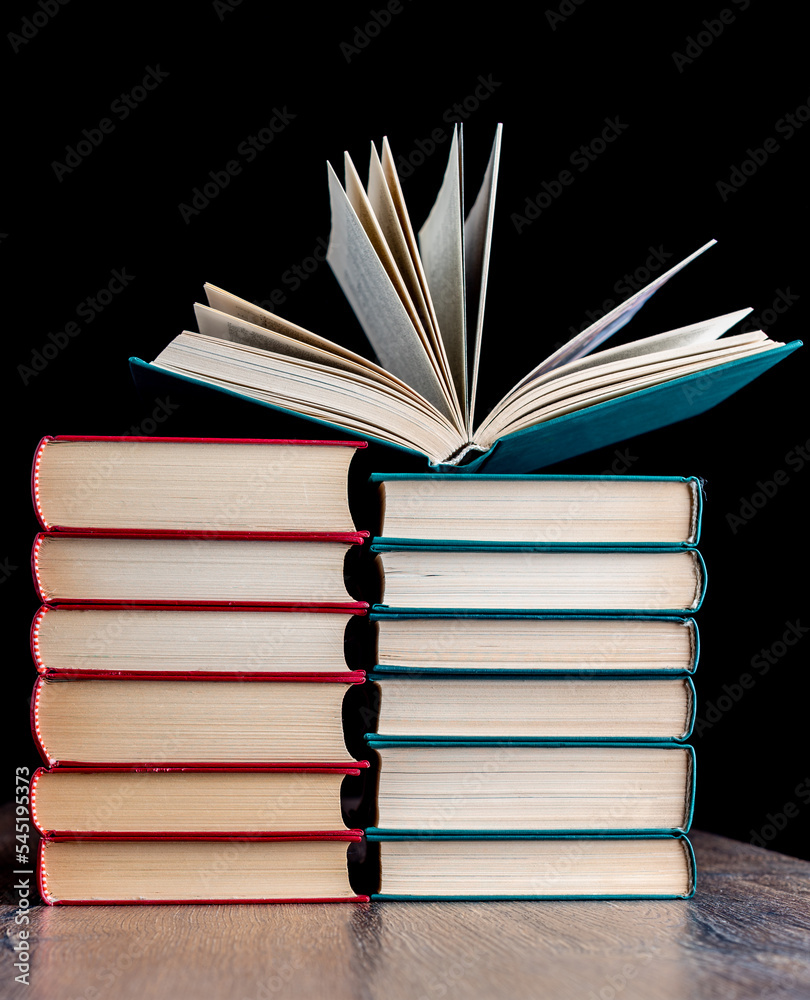 Naklejka premium Two stacks of hardcover paper books and one open.