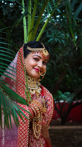 Portrait of a beautiful Indian bride in a traditional wedding dress. Young Hindu woman with golden Kundan jewelry set. Traditional Indian costume lehenga choli.  kalira and red nail paint photo