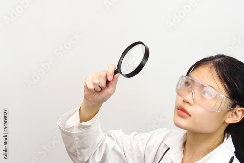 Young female scientist looking something through a magnifying glass.