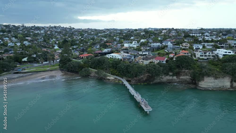 Aerial view zooming out of the shore, seaside houses and a dock at Murrays bay, Auckland Aerial view zooming out of the shore, seaside houses and a dock at Murrays bay, Auckland