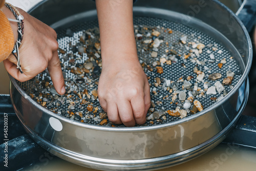 Foto Child hand picking pebbles at the sieve at archaeological excavations or extraction of gold and other gems at the prospecting site
