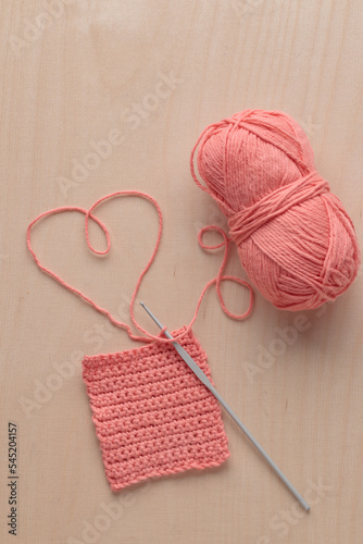Heart Shaped Yarn and Crochet handmade square pattern, pink yarn coil, hook, knitting crocheting top view on a wooden background
