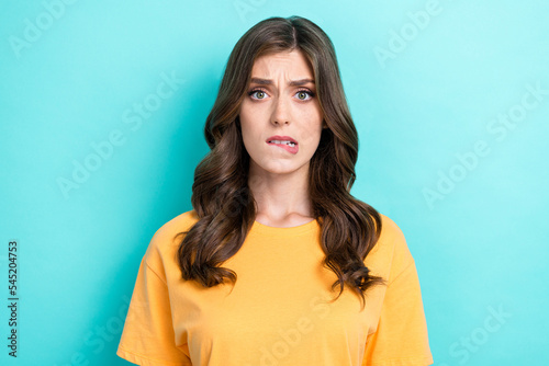 Portrait of unhappy upset worrying girl with curly hairstyle wear yellow t-shirt biting lip isolated on turquoise color background
