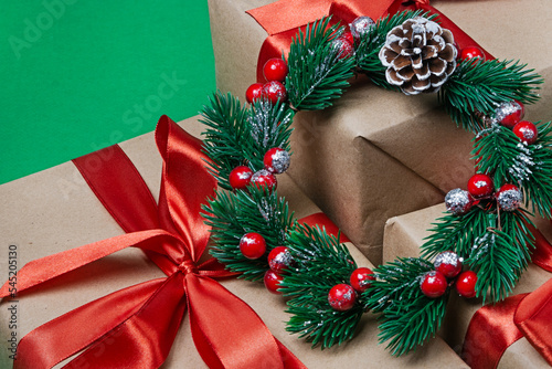 Three New Year's gifts wrapped in brown paper and a Christmas wreath on a green background. Close-up