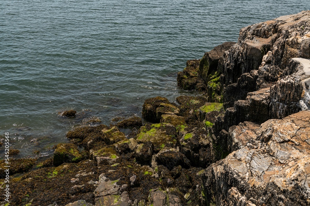 High-angle of mossy rocky cliffs  near the ocean, water waves background