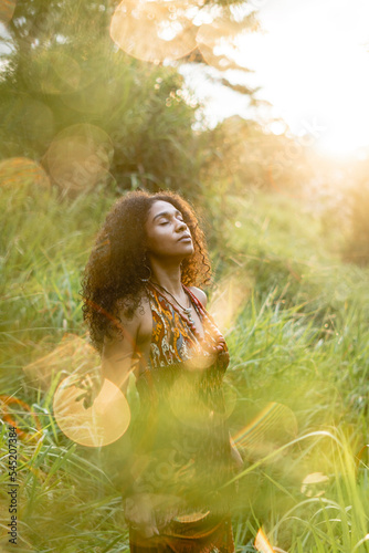 Imagen vertical de una mujer afroamericana sola de pie al aire libre  realizando un ritual de meditación y conexión  con la naturaleza.  photo