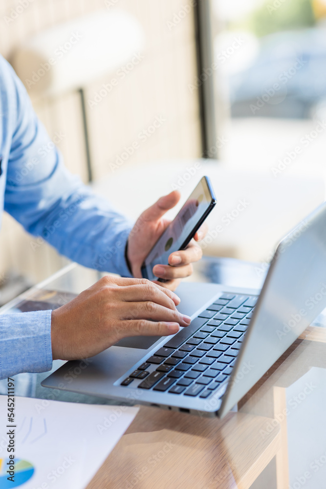 Asian businessmen use equipment for business. Holding a smartphone that works with laptops and mobile phones, showing statistics and software apps. Asian businessmen use equipment for business. Holding a smartphone that works with laptops and mobile phones, showing statistics and software apps.