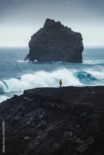 Vertical shot of a person standing on a beach against ocean waves at Reykjanes, Valahnukamol,Iceland photo