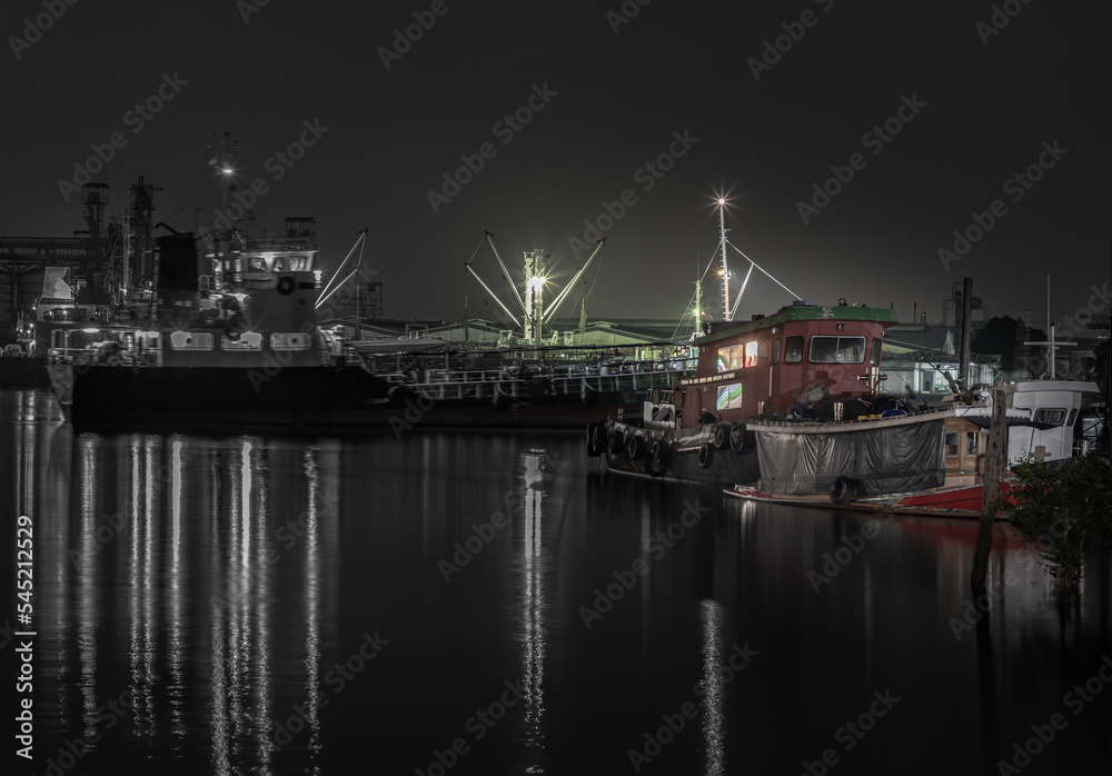 Small harbor with cargo ships and a small boat were parked on the Chao Phraya River at night. Focus and blur.