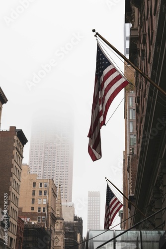 Vertical shot of the American flags hanging from the buildings on a foggy day