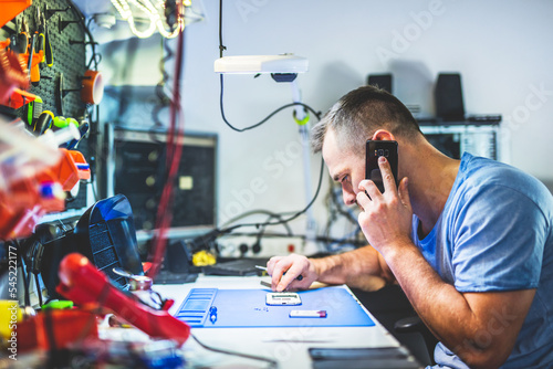 Man speaking on mobile phone repairing electronics in service shop