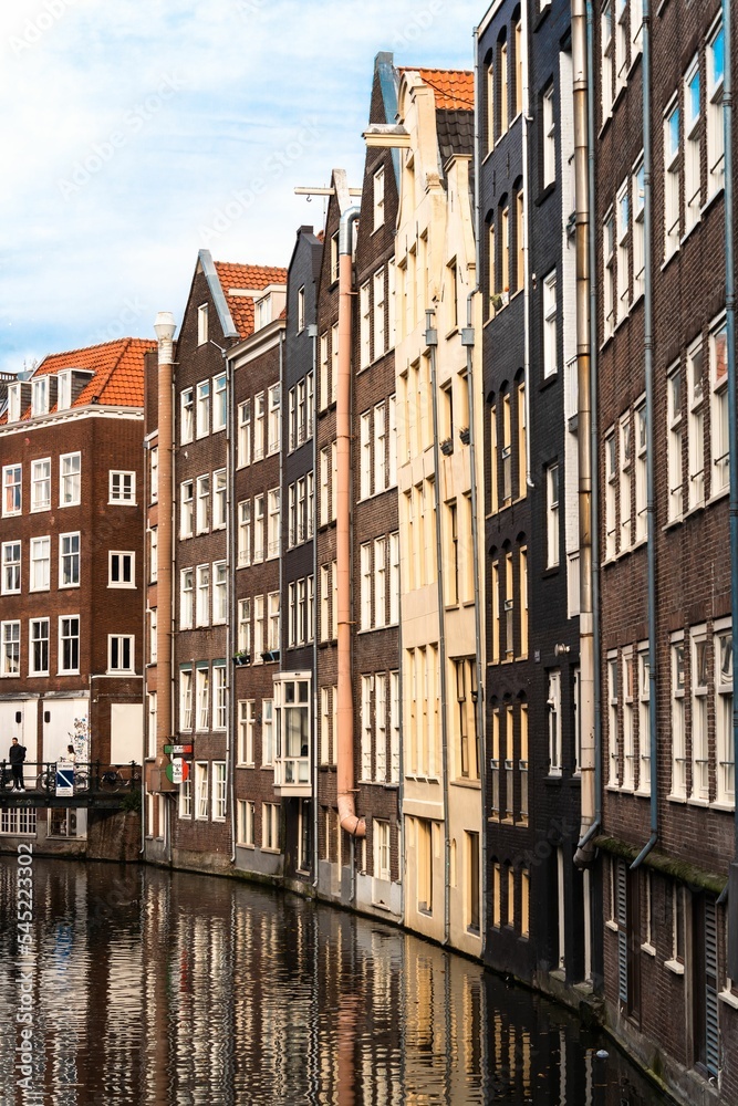 Vertical shot of Damrak avenue buildings in front of a canal, Amsterdam, the Netherlands
