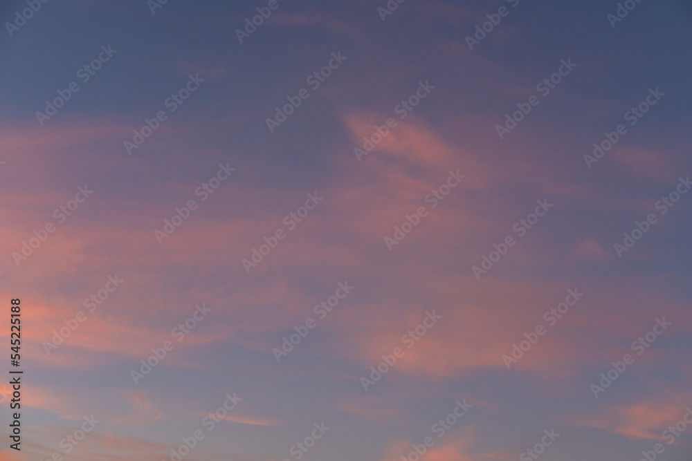 Moody sunset or sunrise sky with rays of light illuminating dark blue and bright and soft pink and orange clouds.
