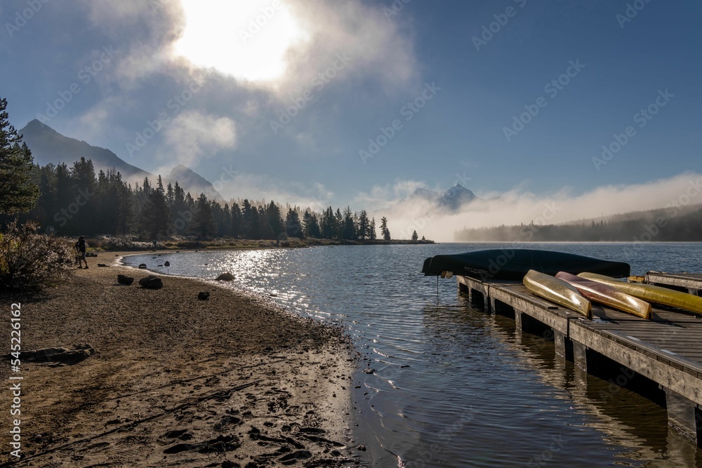 Wooden boardwalk on the seashore with canoes in front of high mountains covered in fog