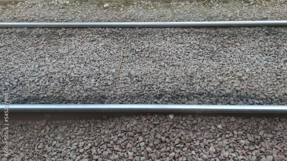Tram rails on brownish gray stones. On dry granite stones scattered with small chips, metal rails for the tram are laid parallel to each other. The camera moves to the right along. Tram rails on brownish gray stones. On dry granite stones scattered with small chips, metal rails for the tram are laid parallel to each other. The camera moves to the right along.