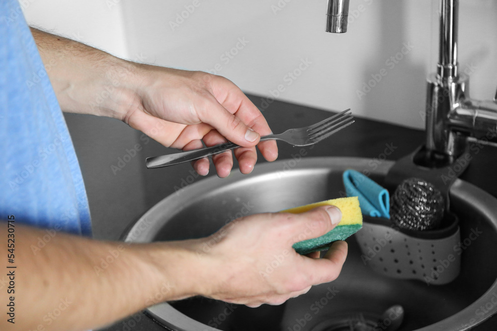 A man washes forks in the sink. Help your wife around the house. A man washes forks in the sink. Help your wife around the house.