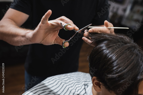 hairdresser cutting hair of brunette teenager in barbershop.