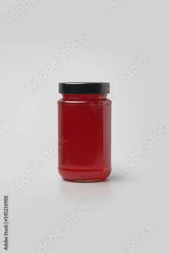 glass jar with bright red jam, bottle with black lid, isolated on neutral gray background, mock-up template
