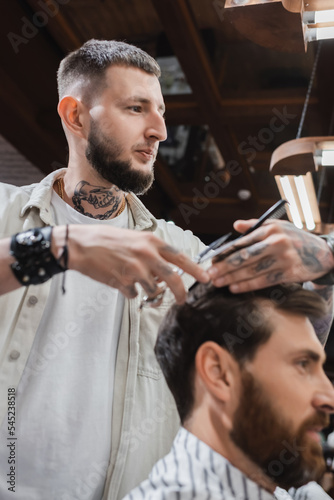 Hairdresser cutting hair of blurred customer in beauty salon.