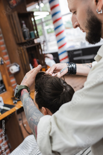Barber touching hair of client during haircut in barbershop.