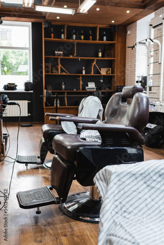 ergonomic armchairs and hairdressing capes in contemporary barbershop.