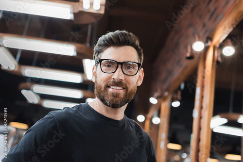 Smiling man in t-shirt and eyeglasses looking at camera in beauty salon.