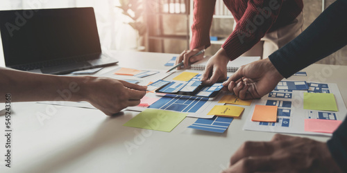 Close up ux developer and ui designer brainstorming about mobile app interface wireframe design on table with customer breif and color code at modern office.Creative digital development agency