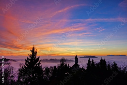 Vibrant sunset over the silhouette of The Church of St. Primoz and Felicijan surrounded by trees