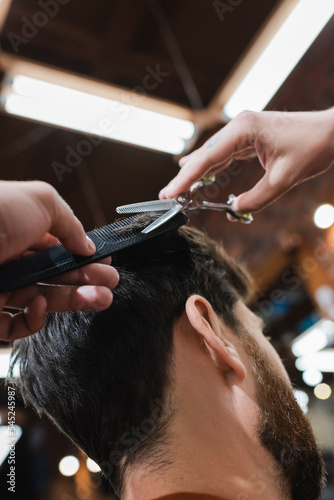 hairdresser cutting hair of brunette man with thinning scissors.