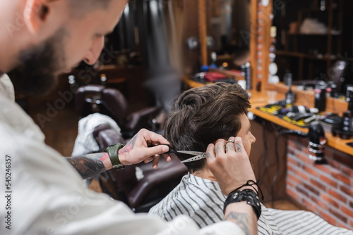 Blurred barber cutting hair of man in hairdressing cape in barbershop.