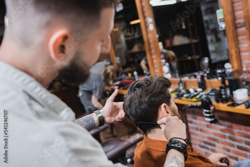 Blurred hairdresser combing hair of man in beauty salon.