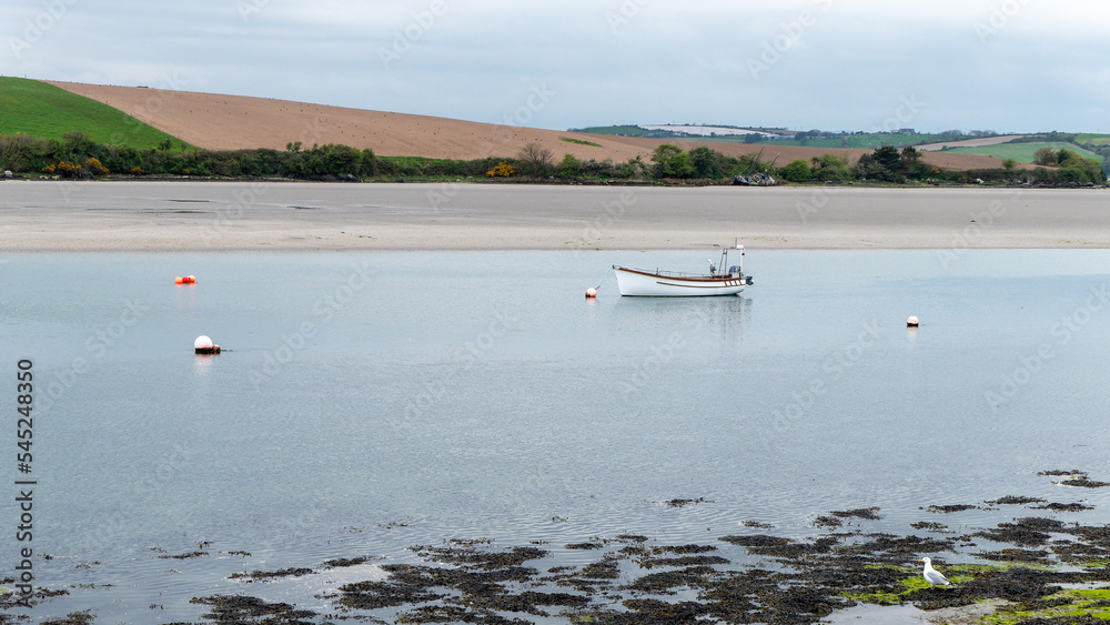 Obraz premium A small motor boat moored in shallow water. Calm water surface. Picturesque hills on the shore of the bay. The sandy shore of the Atlantic Ocean.