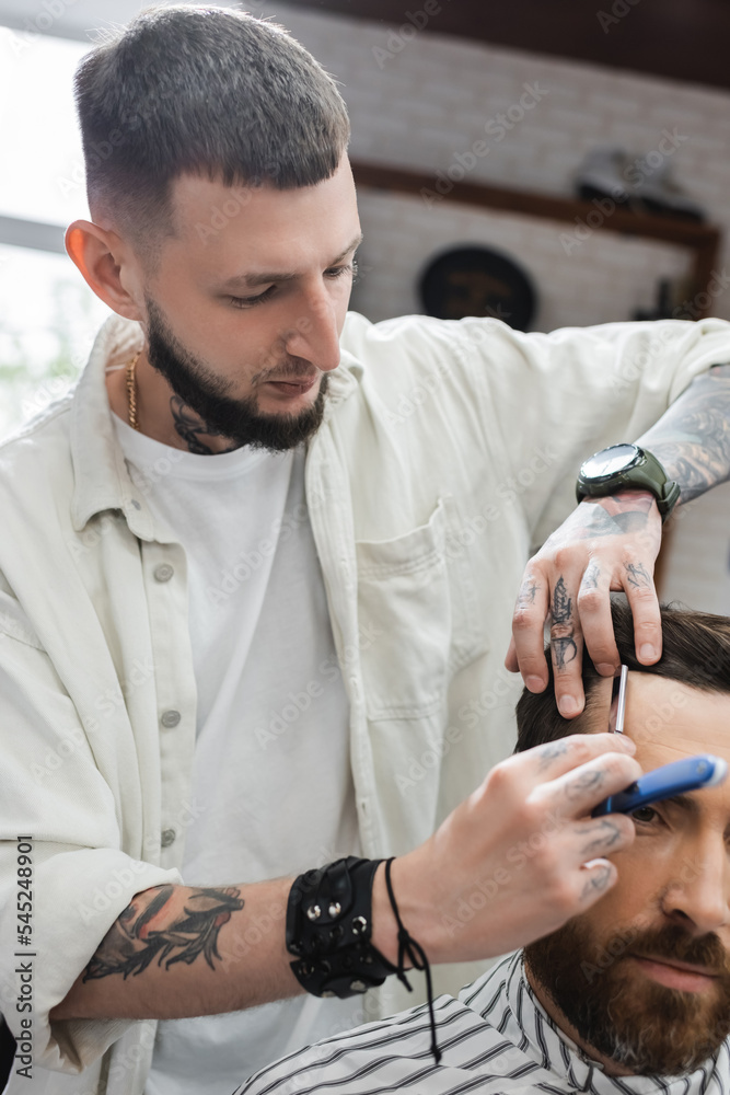 bearded barber shaving forehead of client with straight razor.
