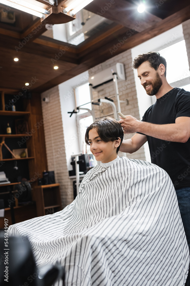 bearded barber working with teenage client sitting in hairdressing cape in beauty salon. bearded barber working with teenage client sitting in hairdressing cape in beauty salon.