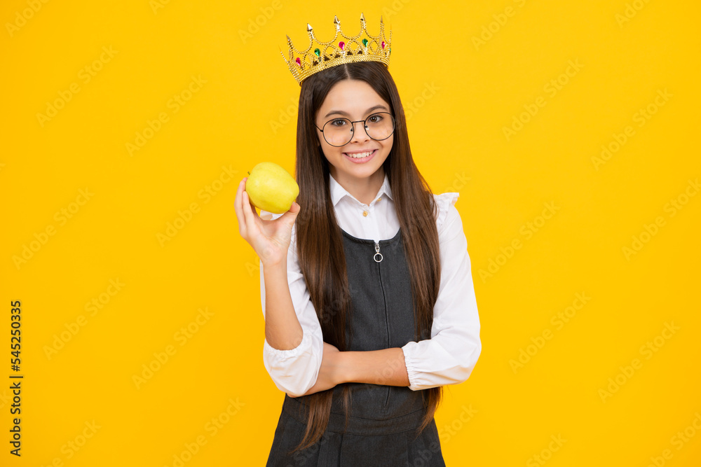 Princess child in queen crown hold apple isolated on yellow background. Teenage girl wear diadem. Happy girl face, positive and smiling emotions.