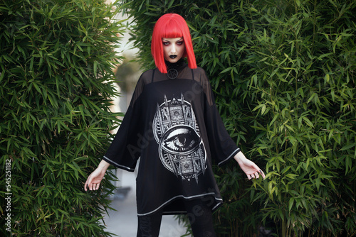 Young urban goth girl with a red hair wig posing outdoors, representing alternative subculture
