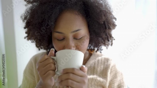 Portrait of young beautiful African American black woman hands holding coffee cup morning spring time in white bedroom. Happy cheerful relaxing in winter. Wakeup university lifestyle concept. photo