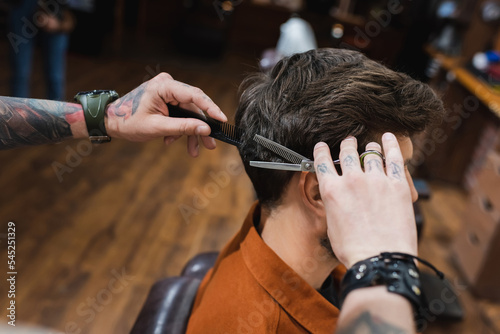tattooed barber cutting hair of brunette man with thinning scissors. © LIGHTFIELD STUDIOS