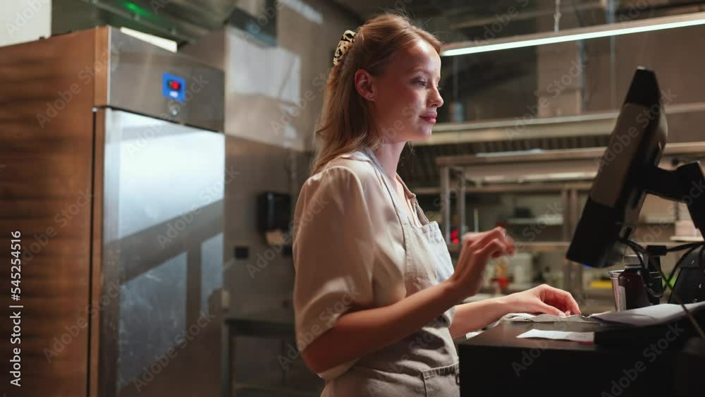 Confident blonde woman cashier typing in the order in the restaurant kitchen