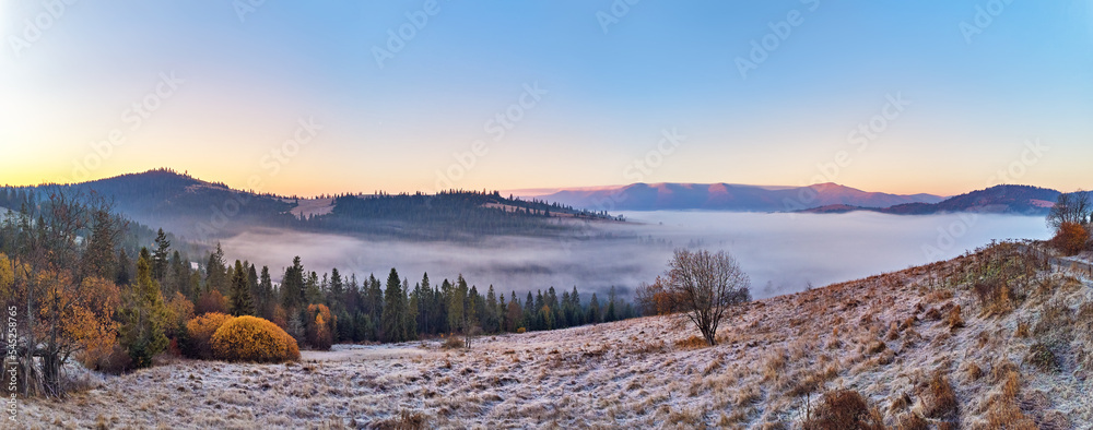 Mountain autumn misty Sunrise panorama. Majestic Morning fog, November Valley Aerial scene. Ice, frost on grass. Fall sunny Landscape, forest hills. Beautiful tonal perspective