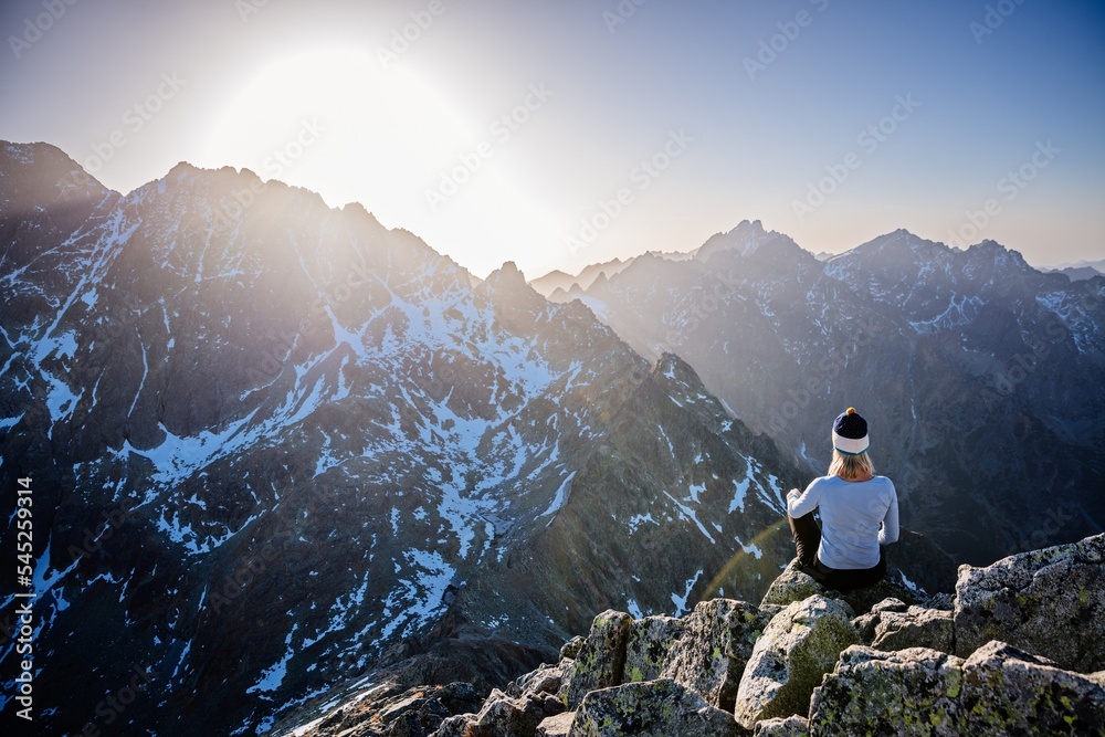 Beautiful blonde woman enjoys reaching the summit in the Slovak Tatras and looks at the Gerlach mountain. Mala Wysoka peak in the Tatra Mountains at sunset. High Tatras, Slovakia