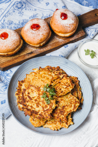 Traditional Jewish festive food for Hanukkah holiday. Jew festival of lights. Potato pancakes Latkes and Sufganiyot jelly doughnuts cooked in oil on white table. Flat lay, top view.