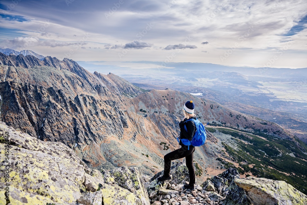 Obraz premium Beautiful blonde woman enjoys the moment while hiking in the Slovak Tatra Mountains on Mount Kryvan. She rests on the route and looks at the lake among the rocky peaks