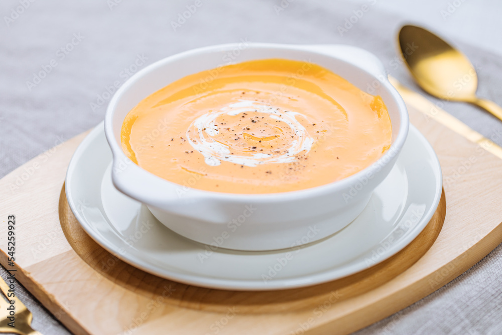 Creamy pumpkin soup garnished with cooking sauce served in turquoise dish with slice of bread in rustic mood. Seasonal warm food. Autumn Appetiser Creamy pumpkin soup garnished with cooking sauce served in turquoise dish with slice of bread in rustic mood. Seasonal warm food. Autumn Appetiser