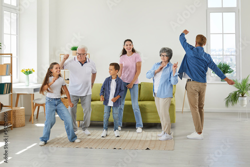 Happy multigenerational family having fun at home. Cheerful, funny mother, father, grandparents and children dancing all together in a light, spacious living room in a big, new house or apartment