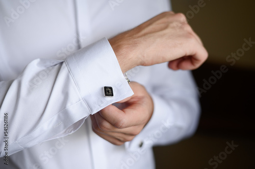 Quadro su tela Portrait of a fashionable man fastening stylish cufflinks on the sleeves of his white shirt