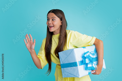Surprised face, surprise emotions of teenager girl. Teenage child holding gift box on blue isolated background. Gift for kids birthday. Christmas or New Year present box.